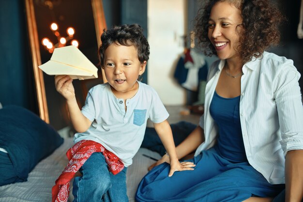 People, childhood, parenting and domesticity concept. Portrait of happy young mixed race female and her cute adorable little son having fun at home