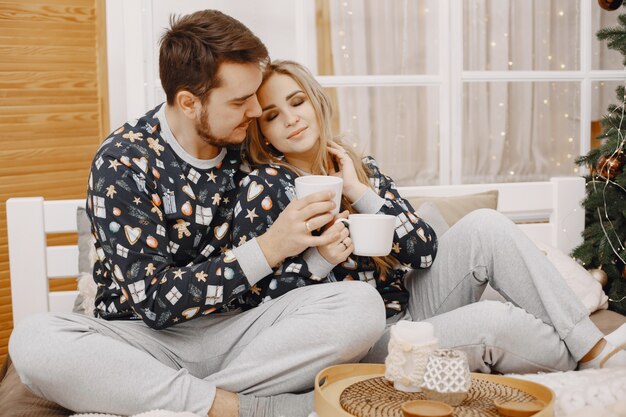 People in a Christman decorations. Man and woman in a identifical pajamas. Family on a bed.