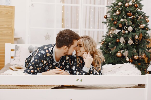 People in a Christman decorations. Man and woman in a identifical pajamas. Family on a bed.