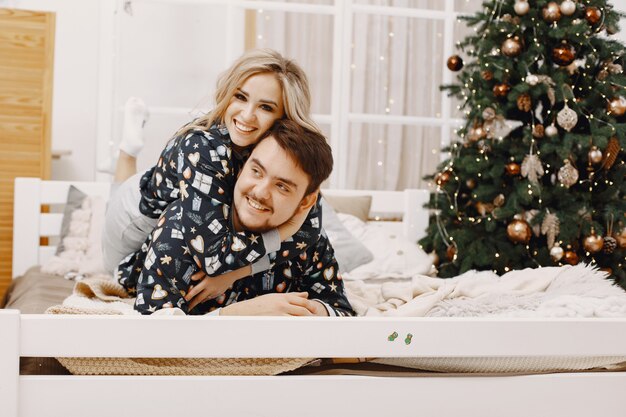 People in a Christman decorations. Man and woman in a identifical pajamas. Family on a bed.