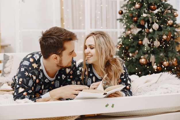 People in a Christman decorations. Man and woman in a identifical pajamas. Family on a bed.