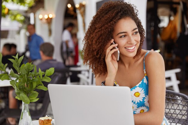 People, communication and technology concept. African American female has pleasant talk with friend via smart phone