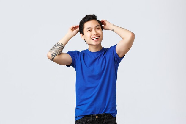 People different emotions, lifestyle and casual concept. Carefree good-looking asian guy happy visited barbershop, touching brand new haircut, smiling pleased, standing grey background.