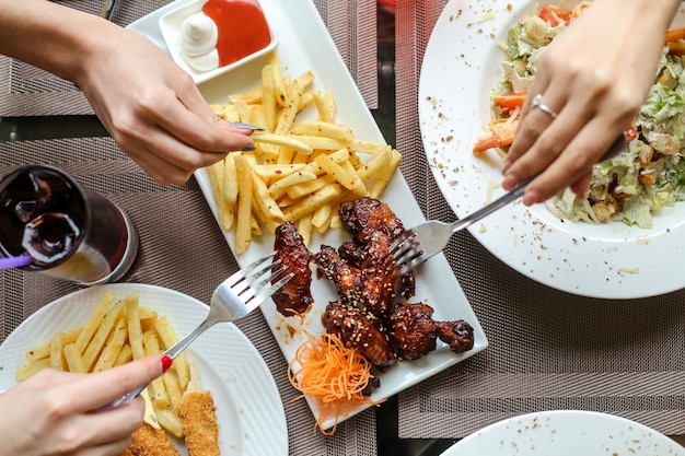 People eating chicken wings with bbq sauce and french fries