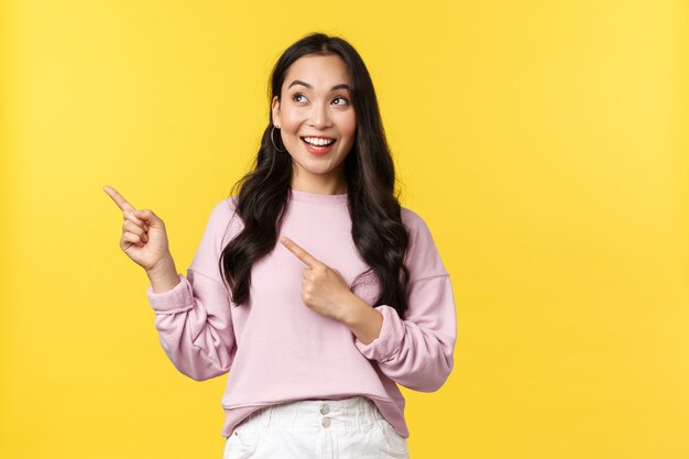 People emotions, lifestyle and fashion concept. Enthusiastic pretty korean woman in stylish outfit pointing upper left corner, showing cool advertisement, special discount offer, yellow background.