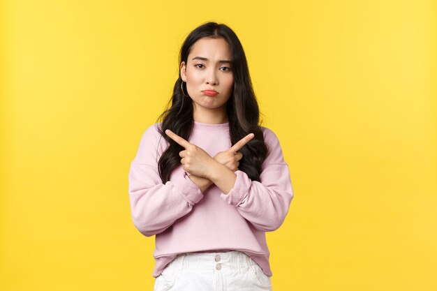 People emotions, lifestyle and fashion concept. Indecisive sad woman troubled making choice, pouting upset and pointing sideways at left and right variants, standing yellow background