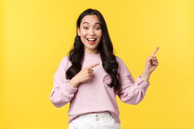 People emotions, lifestyle and fashion concept. Smiling female student showing summer vacation offers, special promo or discounts at store, pointing fingers right and smiling, yellow background.