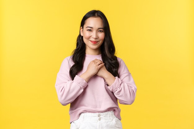 People emotions, lifestyle and fashion concept. Touched lovely korean woman looking flattered and delighted, holding hands on heart and smiling, receive gift, standing yellow background.
