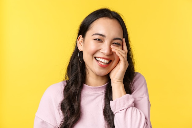 People emotions, lifestyle leisure and beauty concept. Beautiful asian girl touch face and laughing with happy cheerful smile, hear compliment and blushing, stand yellow background.