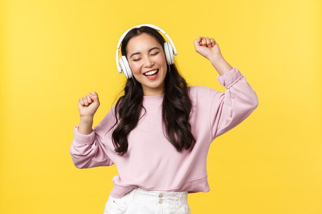 People emotions, lifestyle leisure and beauty concept. Joyful pretty asian woman in wireless headphones listening music, dancing excited with closed eyes and happy smile, listen favorite song.