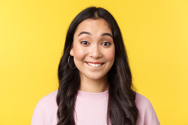 People emotions, lifestyle leisure and beauty concept. Upbeat happy asian girl anticipating big event or surprise, biting lip tempting see, standing yellow background excited.