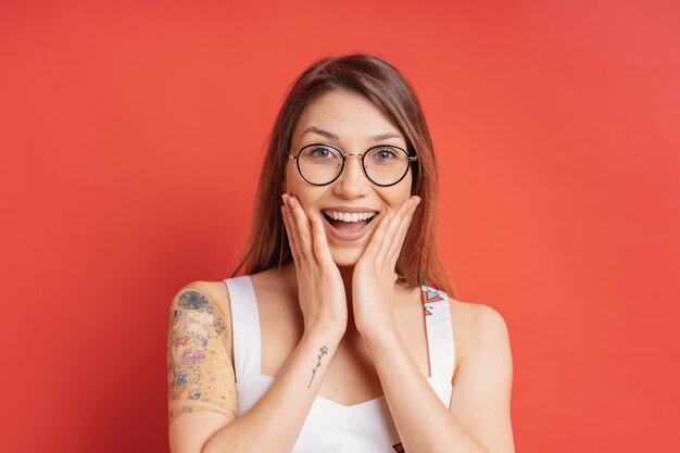 People emotions - portrait of surprised positive girl over red wall