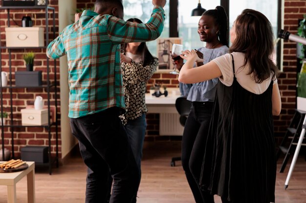 People enjoying fun time together with alcoholic beverages and crazy disco dance moves. Happy multicultural friends listening to funky music while drinking wine and having fun at wine party.