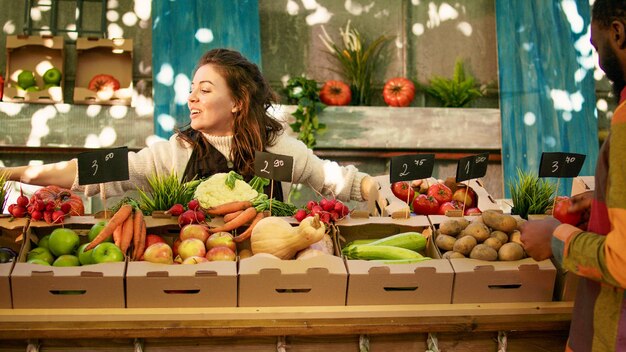 People enjoying shopping at local farmers market, checking fresh farm produce. Young diverse couple standing at farming stand with various homegrown organic fruits and vegetables.