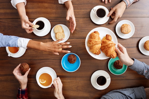 people hands on wooden table with croissants and coffee.
