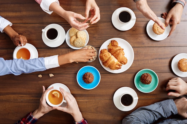 people hands on wooden table with croissants and coffee.