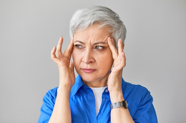 People, health, stress, age and maturity concept. Isolated shot of frustrated frowning European fifty year old woman having high blood pressure, massaging temples to soothe intolerable pain