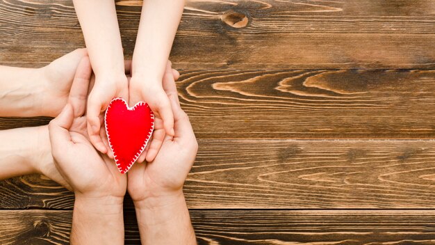 People holding a red heart in hands with copy space