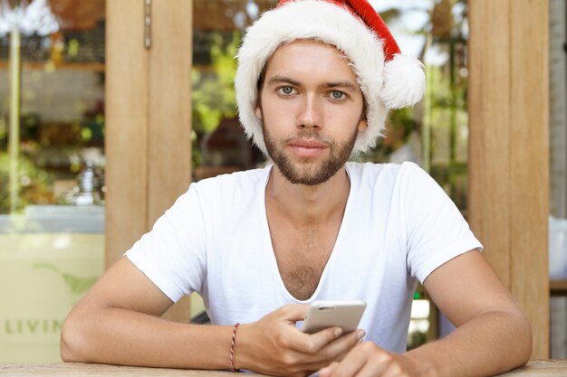 People, holidays, technology and communication. Young hipster with stylish beard using free wi-fi on cell phone