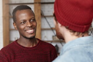 People, interracial friendship and communication concept. handsome cheerful young afro-american man dressed in cozy sweater smiling happily rejoicing at that his caucasian friend got married