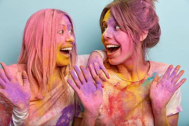 사람, 기쁨, 축하 개념. 즐거운 젊은 여성의 초상화는 행복하게 서로를 응시하고 힌두교에서 가장 다채로운 행사를 기뻐하고 적극적으로 몸짓을하며 몸에 색 가루가 있습니다.