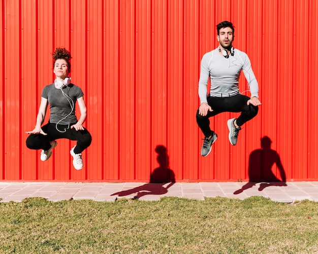 무료 사진 빨간 벽 근처 점프하는 사람들