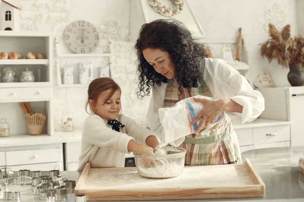 People in a kitchen. Grandmother with little daughter. Adult woman teach little girl to cook.