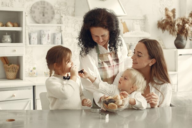 People in a kitchen. Grandmother with little grandchildren. Children eats cookies.