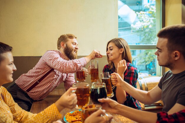 人、レジャー、友情、コミュニケーションコンセプト-ビールを飲みながら幸せな友達がバーやパブで話してチャリンというグラス