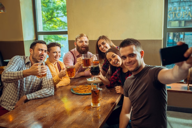Люди, отдых, дружба и общение концепция - счастливые друзья пили пиво, разговаривали и чокались в баре или пабе