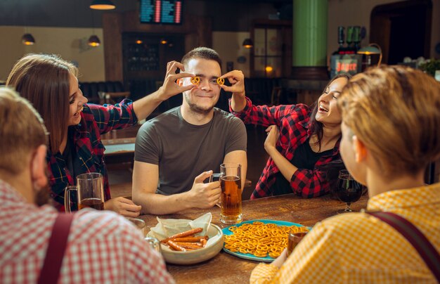 Люди, отдых, дружба и общение концепция - счастливые друзья пили пиво, разговаривали и чокались в баре или пабе
