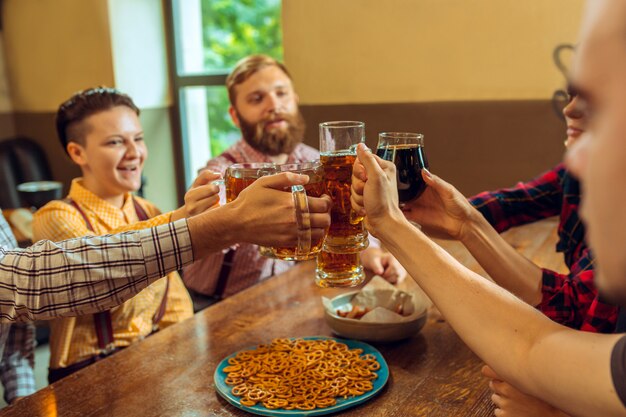 人、レジャー、友情、コミュニケーションコンセプト-ビールを飲みながら幸せな友達が話しているとバーやパブでグラスをチャリンという音