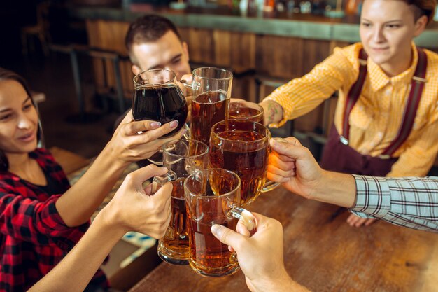 People, leisure, friendship and communication concept - happy friends drinking beer, talking and clinking glasses at bar or pub