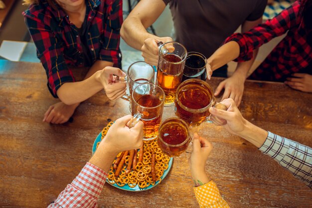 人、レジャー、友情、コミュニケーションコンセプト-ビールを飲みながら幸せな友達が話しているとバーやパブでグラスをチャリンという音
