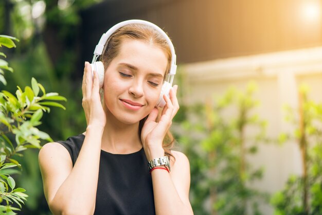 人々のレジャーと技術の概念 - 屋外で音楽プレーヤーで音楽を聴く魅力的な若い女性。朝の公園で彼女のイヤホンの曲を楽しむヒップスターの女の子。レンズフレア。