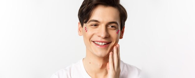 People lgbtq and beauty concept headshot of beautiful gay man with glitter on face smiling and looki