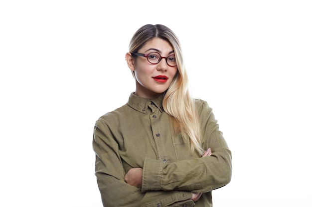 People and lifestyle concept. Horizontal shot of beautiful young blonde female of Caucasian appearance wearing fashionable eyeglasses and denim green shirt posing with arms folded