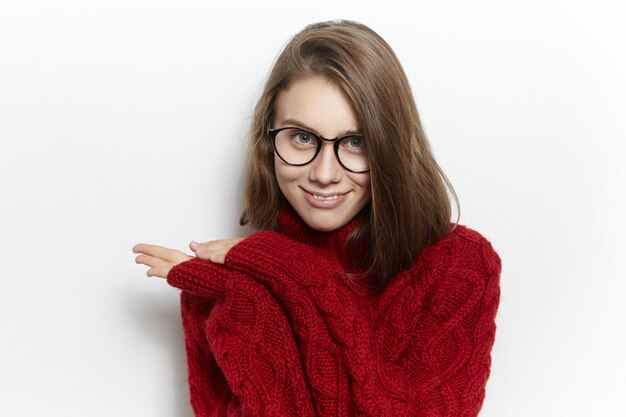 People and lifestyle concept. Picture of gorgeous fashionable young Caucasian woman with loose hair posing, wearing knitted maroon pullover with long sleeves, having mysterious look
