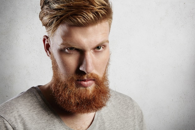 Free photo people and lifestyle. headshot of handsome hipster with thick red beard and stylish hair   with serious face expression, squinting his eyes.