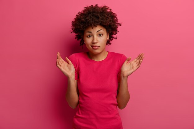 People, lifestyle, perception concept. Questioned bewildered Afro American woman stands unsure, shrugs shoulders, cannot give answer on difficult question, has perplexed expression, stands indoor