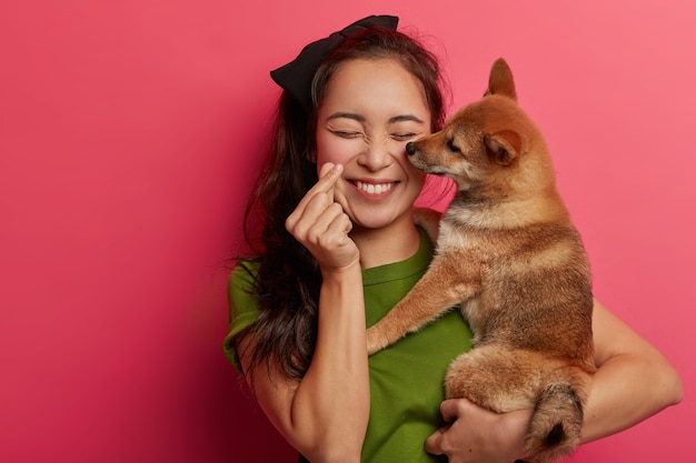 People, love to animals concept. Positive korean girl plays with shiba inu dog, makes mini heart hand gesture