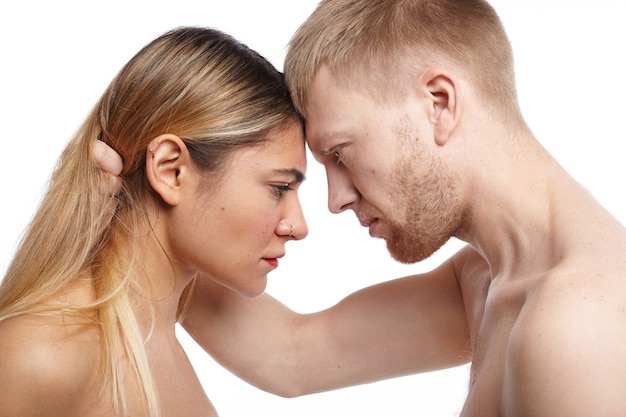 People, love, intimacy, sex and relationships concept. Sideways shot of passionate shirtless European bearded man grabbing hair of his attractive topless girlfriend and staring at her with passion