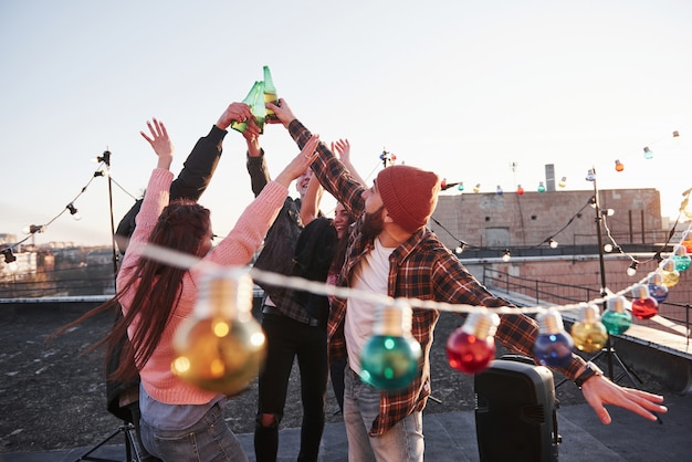 People make a toast. Holidays on the rooftop. Cheerful group of friends raised their hands up with alcohol