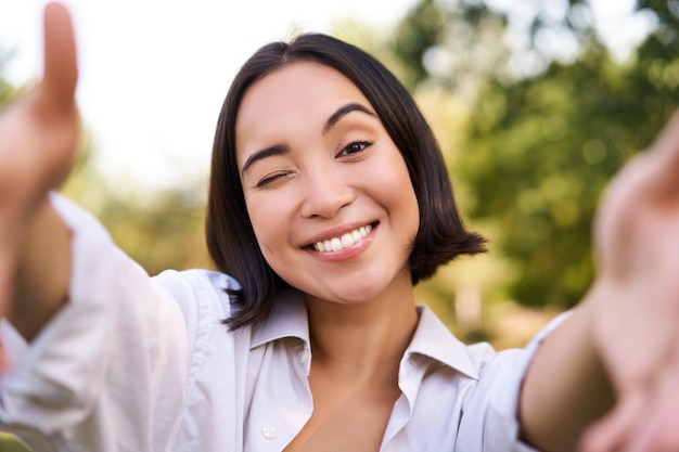 Free photo people and mobile connection happy young asian woman takes selfie on smartphone holds camera with ha