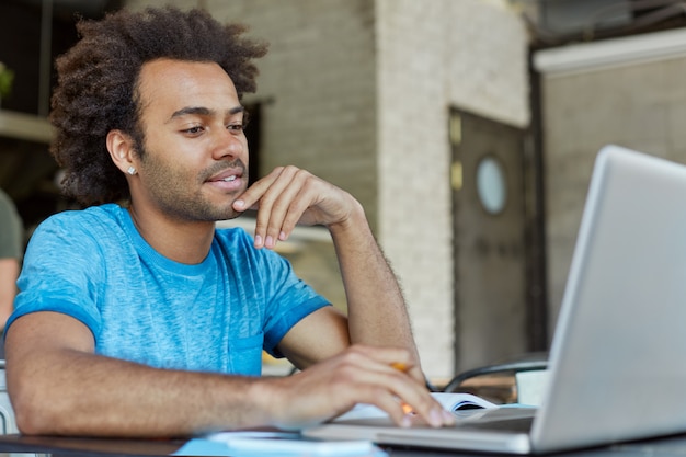 People, modern technology, education, learning and knowledge concept. handsome confident young afro american man sitting in front of open laptop, studying, taking online course on modern art