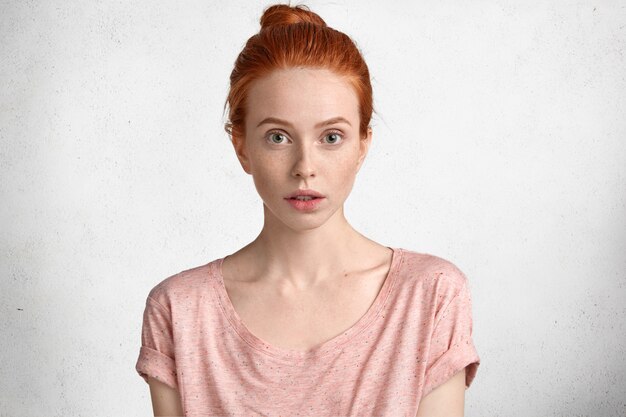 Бесплатное фото Люди, понятие естественной красоты. серьезная привлекательная молодая женщина с жадными глазами и рыжими волосами, одетая в повседневную розовую футболку, сосредоточена на чем-то впереди