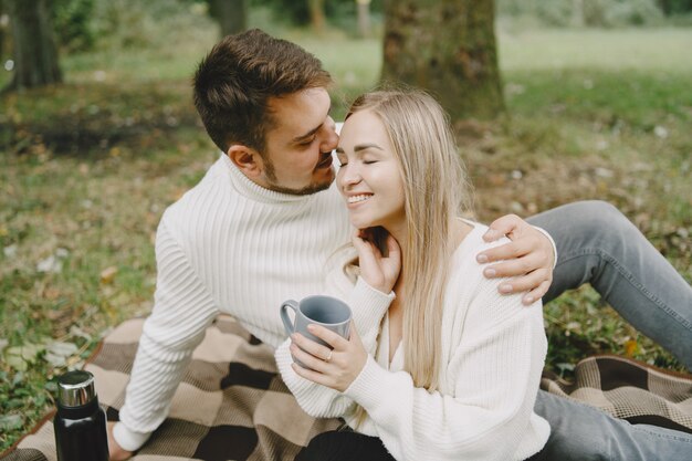 People in a park. Woman in a brown coat. Man in a white sweater. Couple in a picnic.