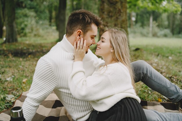 People in a park. Woman in a brown coat. Man in a white sweater. Couple in a picnic.