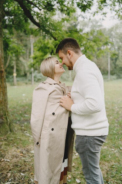 People in a park. Woman in a brown coat. Man in a white sweater.