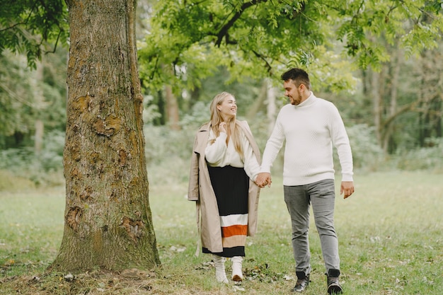 People in a park. Woman in a brown coat. Man in a white sweater.